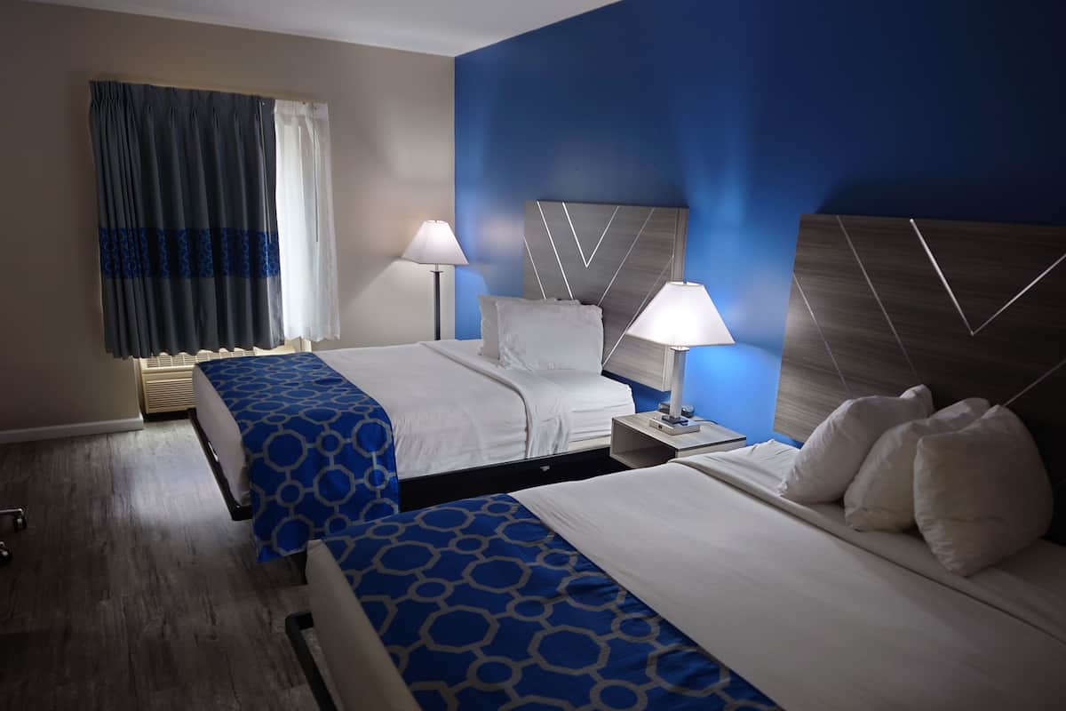 Habitación de hotel con dos camas, una mesita de noche, una lámpara y una ventana con cortinas.