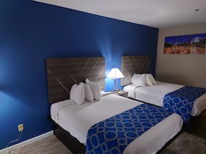 A hotel room with two beds, a nightstand with a lamp, and a wall with a cityscape painting. - Baymont by Wyndham Adairsville (Adairsville)