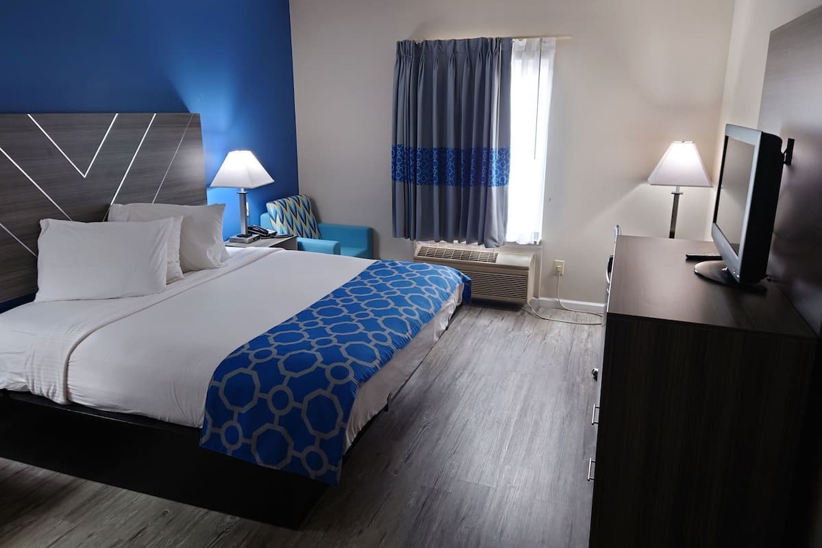 Habitación de hotel con cama, mesitas de noche, escritorio, silla, televisor y ventana con cortinas.