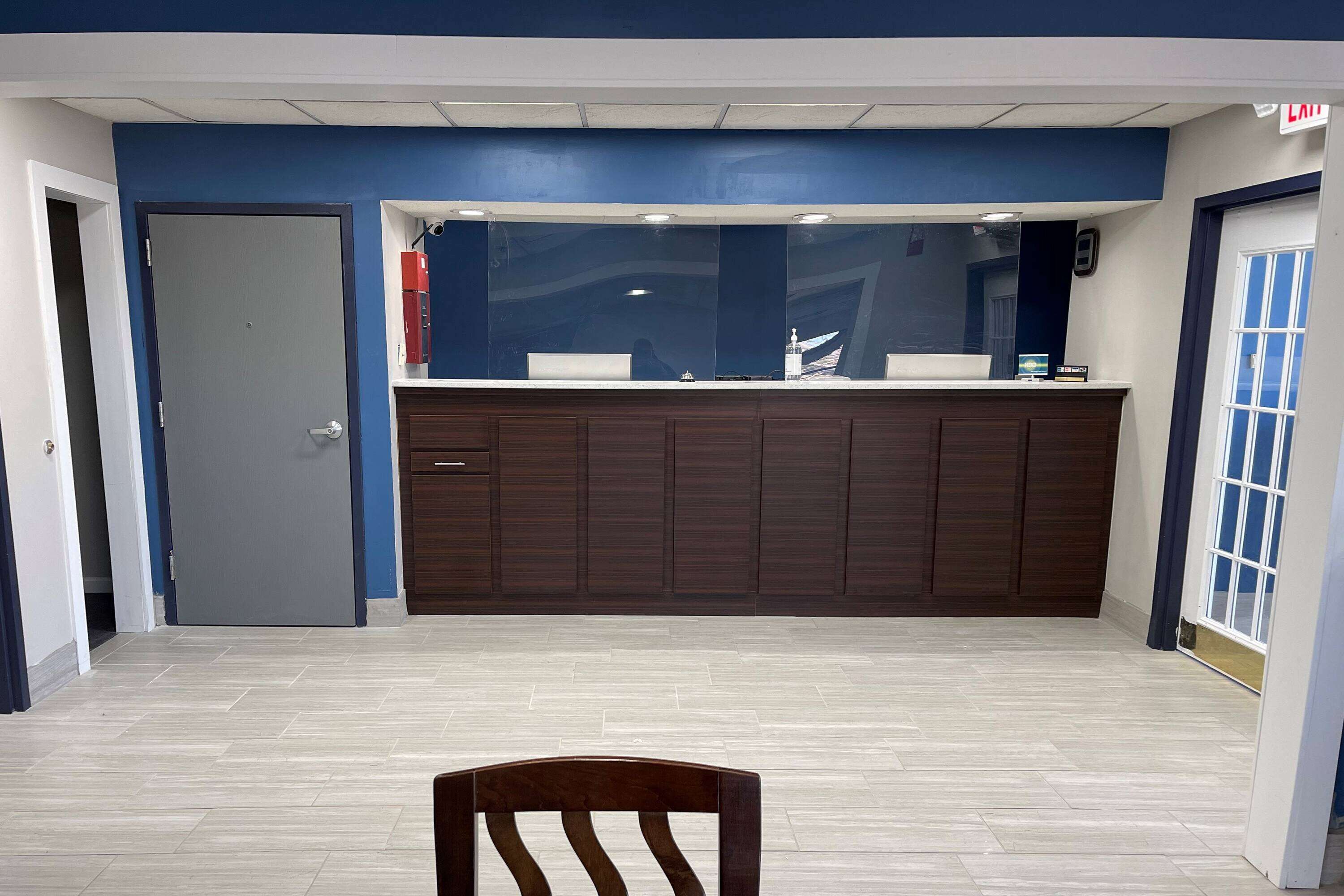 Uma área de recepção com um balcão de madeira escura, uma parede azul decorativa e piso de azulejos.