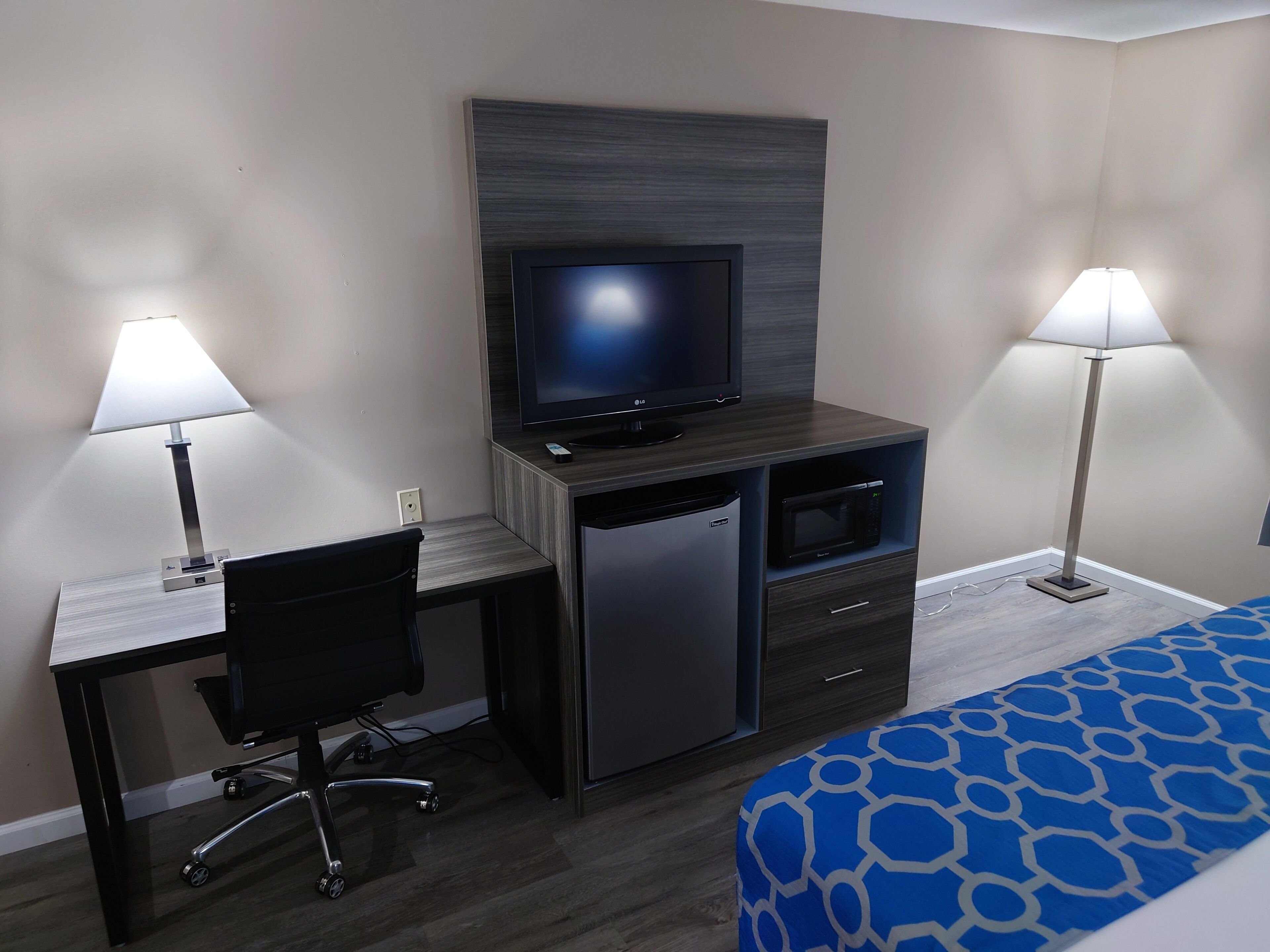 A hotel room with a desk, chair, television, microwave, and bed.