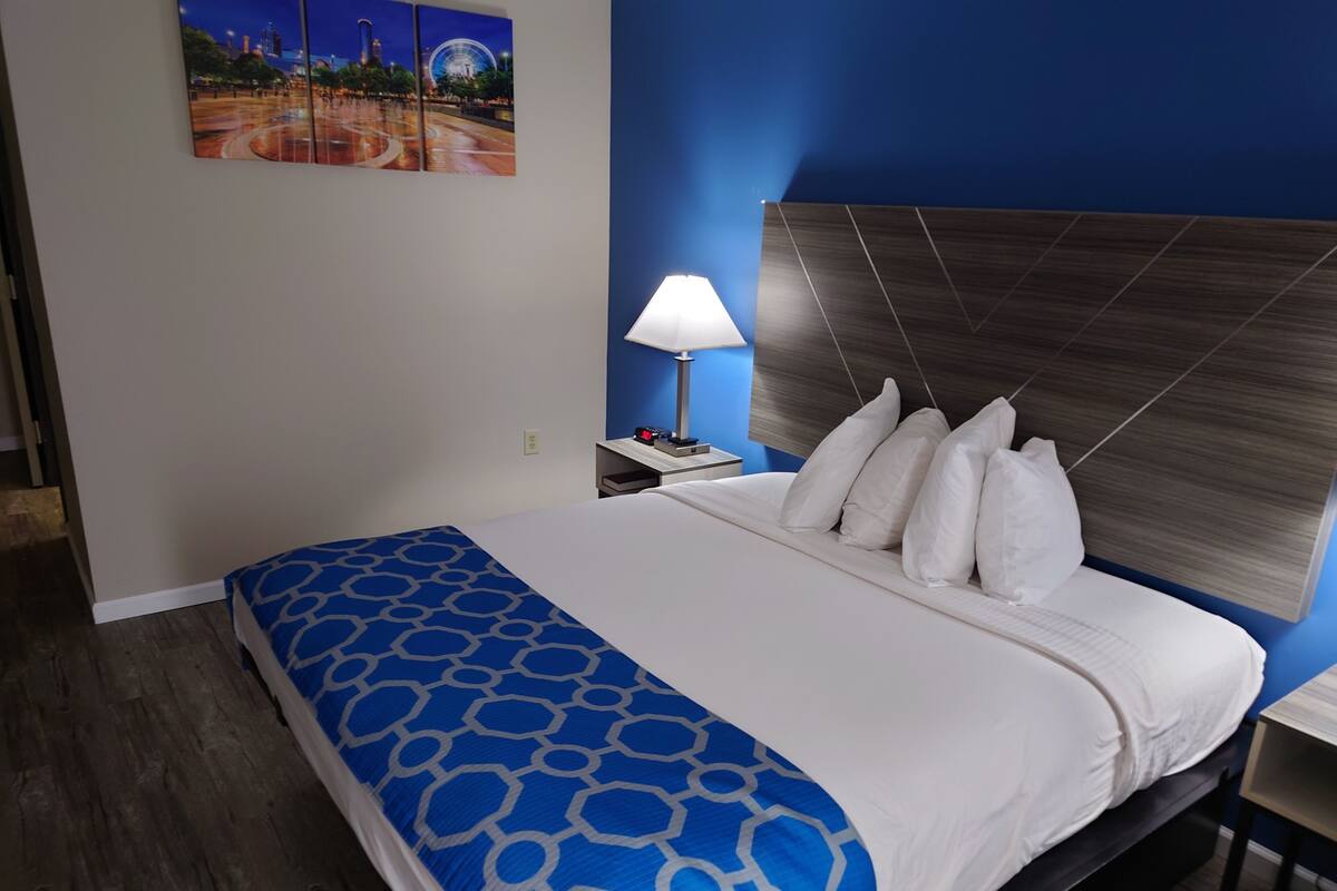 Una habitación de hotel con cama, mesita de noche, lámpara y una obra de arte colgada en la pared.