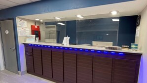 Un mostrador de recepción con un cartel de registro de entrada/salida, una pantalla digital y un dispensador de agua.