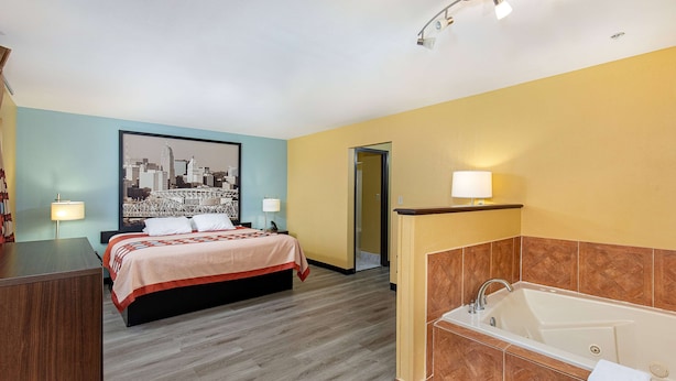 A hotel room with a bed, a bathroom with a bathtub, and a cityscape painting on the wall.