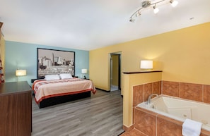 A hotel room with a bed, a bathroom with a bathtub, and a cityscape painting on the wall.