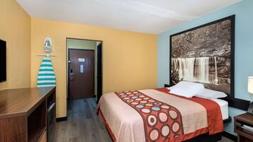 Habitación de hotel con cama, escritorio, silla, puerta y pared decorada con una pintura de cascada.