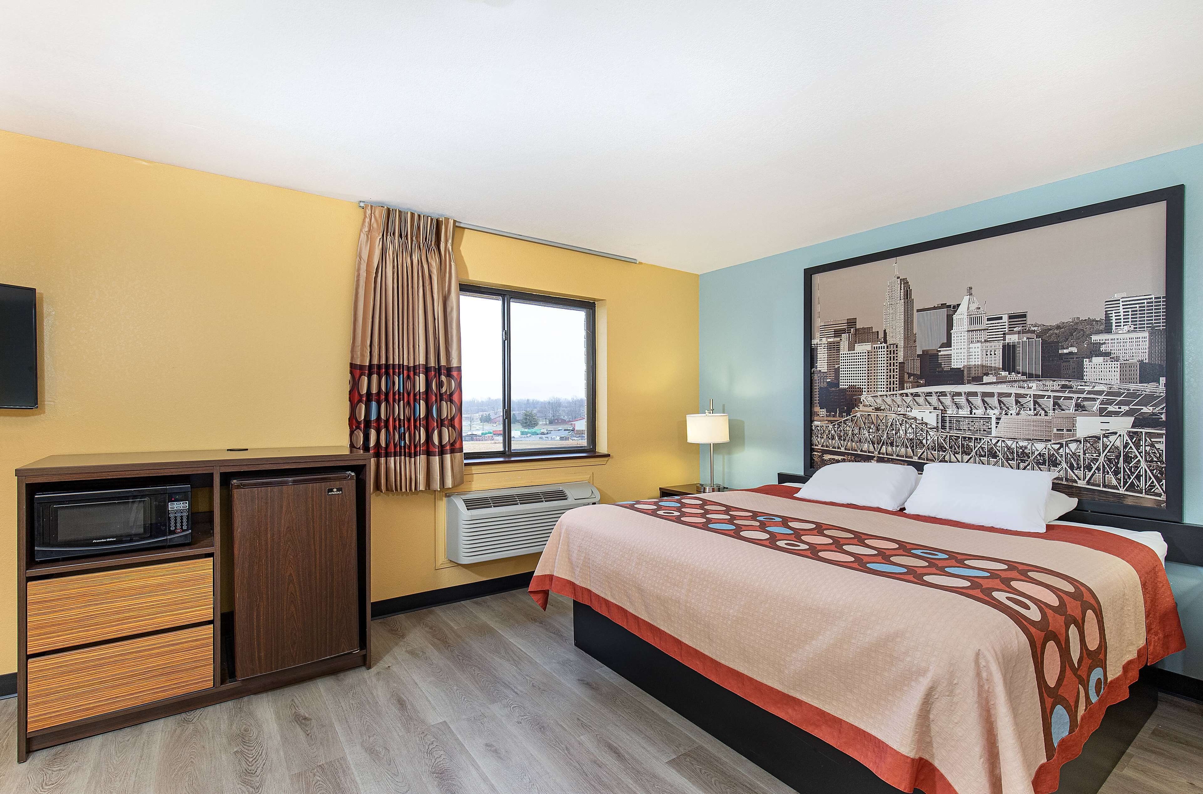 Habitación de hotel con cama, una kitchenette pequeña con microondas, calefacción y una ventana con cortinas.