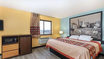 Habitación de hotel con cama, una kitchenette pequeña con microondas, calefacción y una ventana con cortinas.