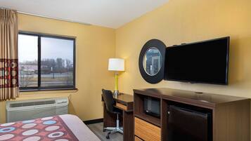 Een hotelkamer met een bed, bureau, stoel, televisie en een raam met gordijnen.