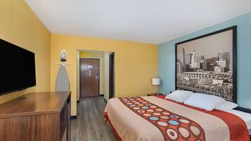 A hotel room with a bed, a television, a desk, and a cityscape painting on the wall.