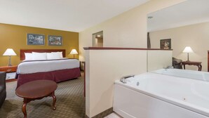 A hotel room with a bed, a sitting area, a large bathtub, and a mirror. - Days Inn by Wyndham Norton (Norton)