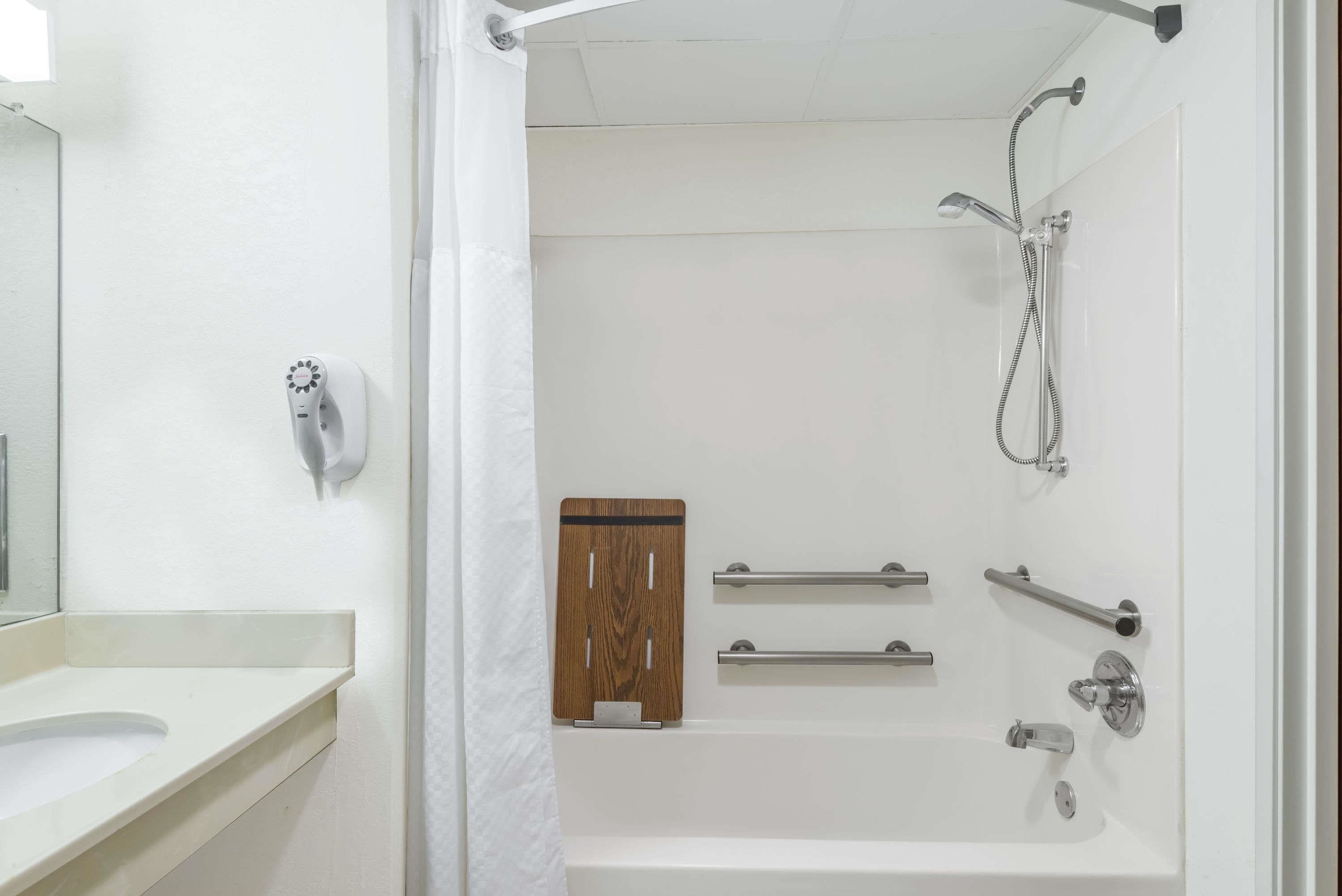 Un baño con lavamanos blanco, espejo, ducha con cabezal de ducha manual y un panel de madera en la pared.
