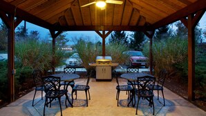 Une terrasse extérieure dotée d’un ventilateur de plafond, d’un barbecue et de six chaises disposées autour d’une table.