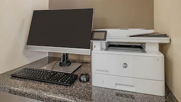 Um computador de mesa com monitor, teclado e rato, sobre uma bancada de granito, ao lado de uma impressora.