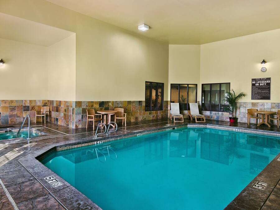 Una piscina con sillas de descanso y una pequeña mesa, rodeada por un muro de azulejos y un letrero que indica que no hay socorrista de servicio.