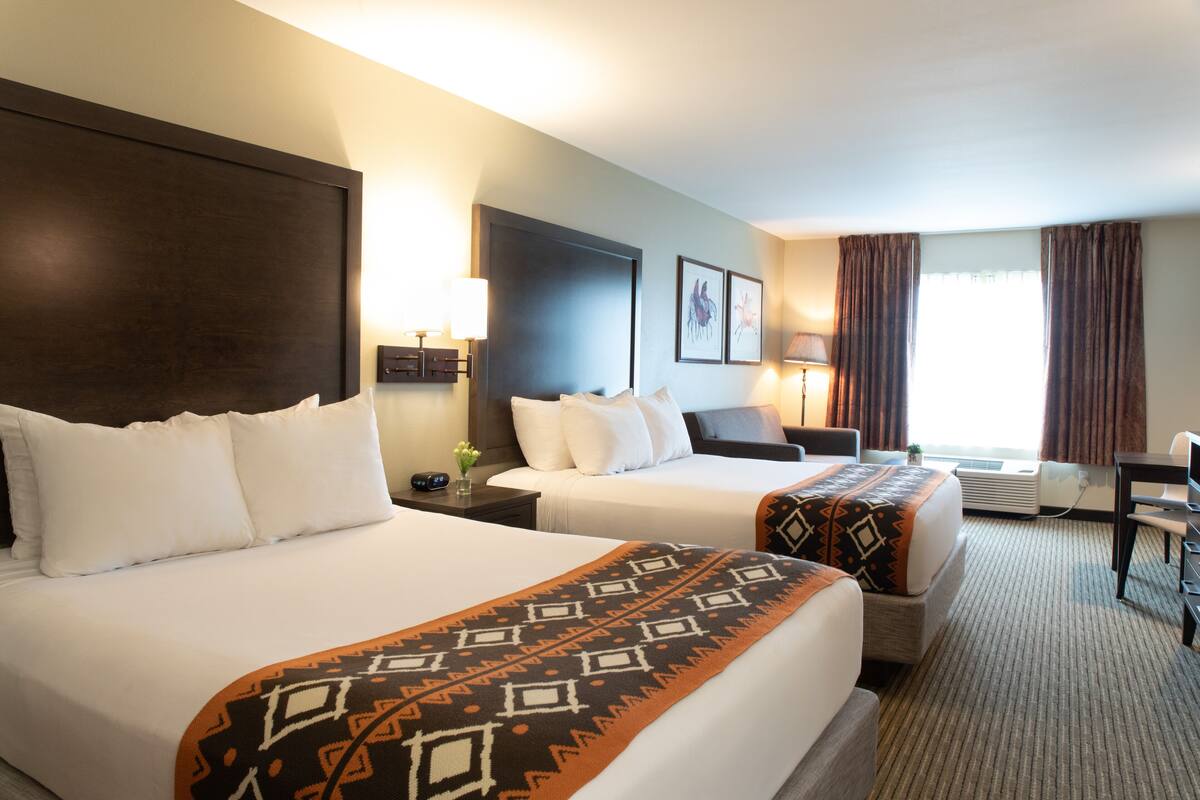 A hotel room with two beds, a desk, a chair, and a window with curtains.