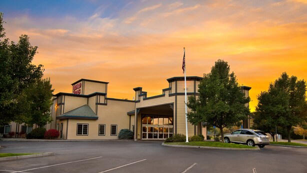 A hotel with a large parking lot, a flagpole, and a building with a sign.