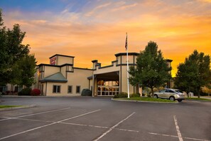 A hotel with a large parking lot, a flagpole, and a building with a sign.