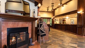 A hotel lobby with a fireplace, wooden flooring, and a seating area with a checkered blanket.