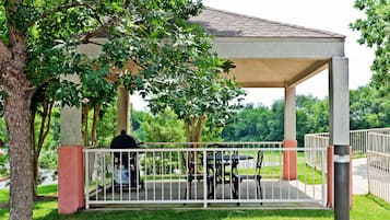 A covered outdoor patio with a grill, seating, and a white fence.