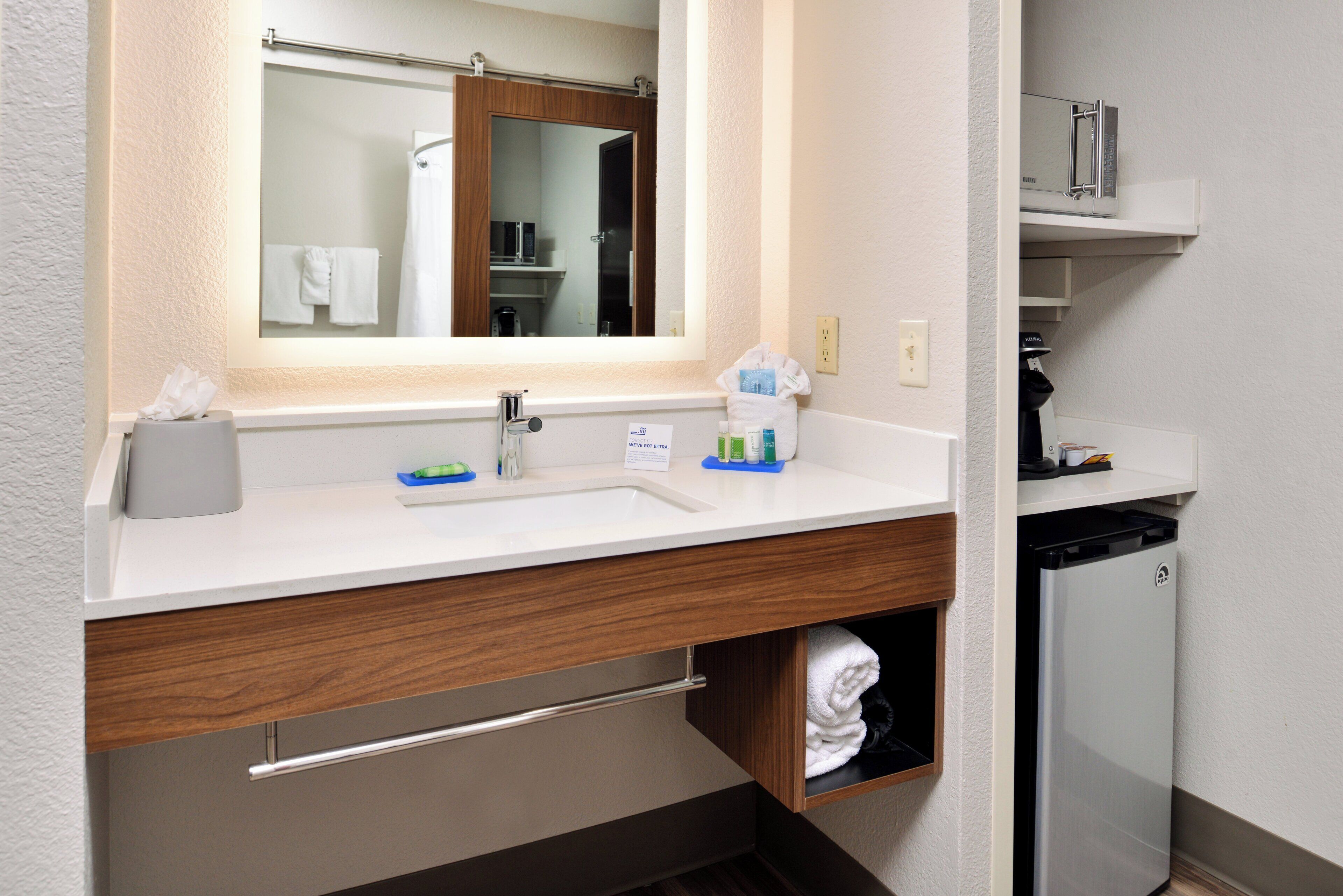 A hotel bathroom with a sink, mirror, towel rack, and a trash bin.
