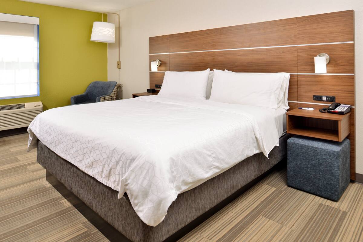A hotel room with a large bed, a chair, a nightstand with a phone, and a lamp.