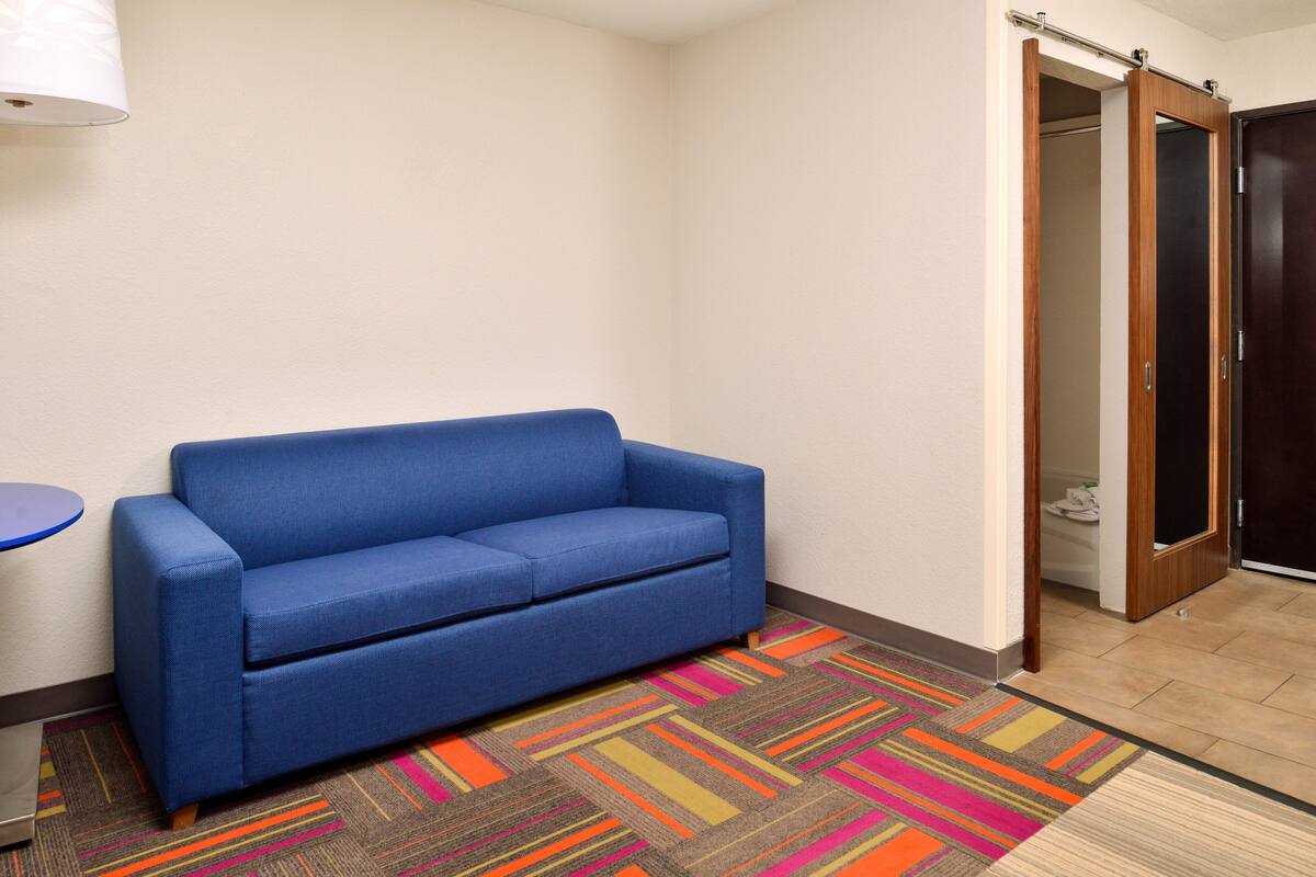 A blue sofa in a corner, a colorful striped carpet, and a wooden door.