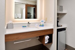 A bathroom with a white sink, a mirror, a towel rack, and a small shelf with toiletries. - Holiday Inn Express & Suites North Kansas City by IHG (North Kansas City)