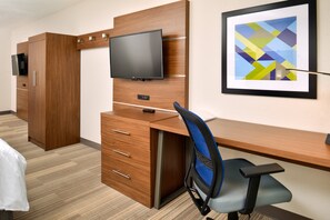 A hotel room with a wooden desk, a television mounted on the wall, and a framed abstract painting. - Holiday Inn Express & Suites North Kansas City by IHG (North Kansas City)