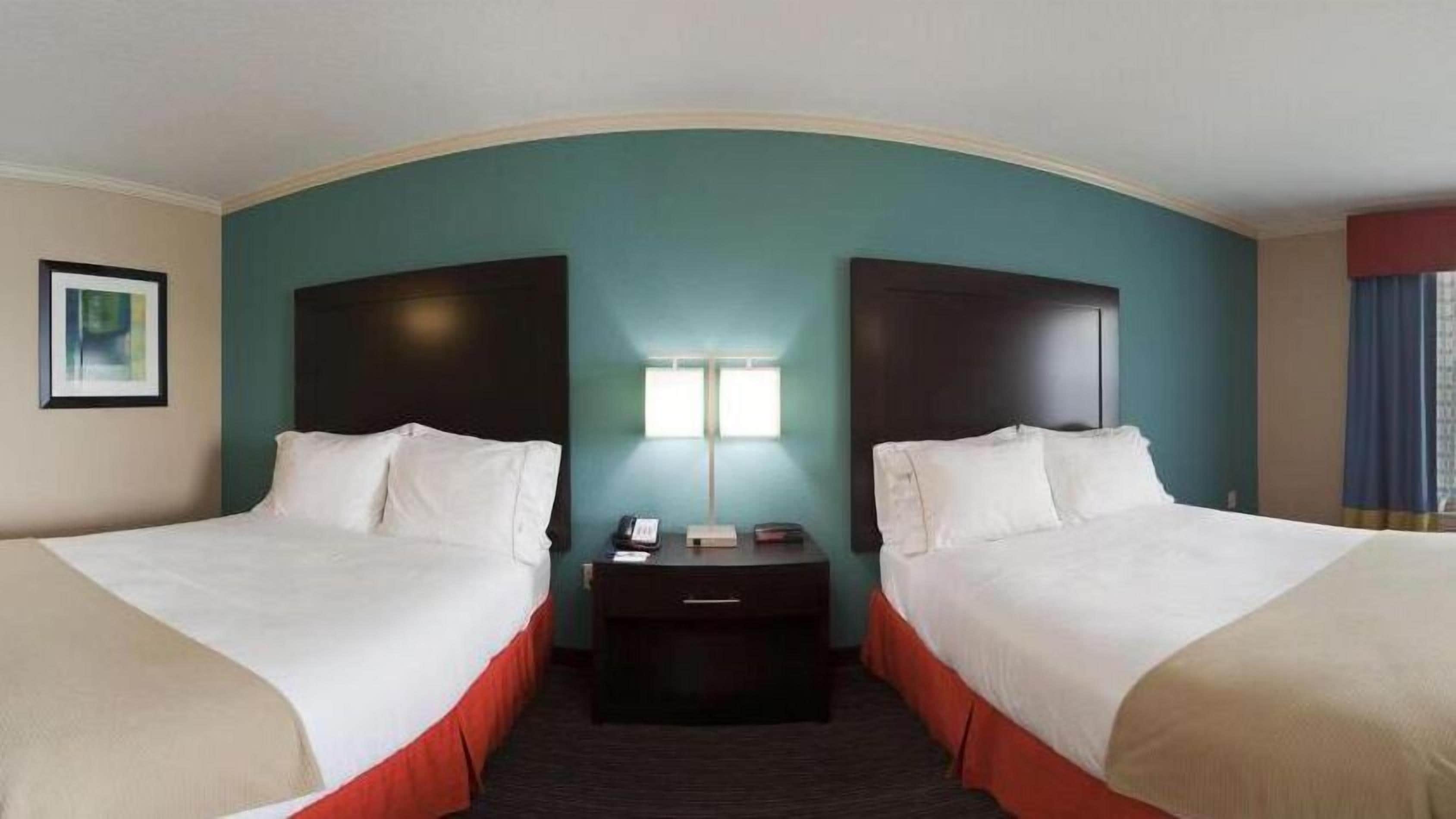 A hotel room with two beds, a nightstand, a lamp, and a framed picture on the wall.
