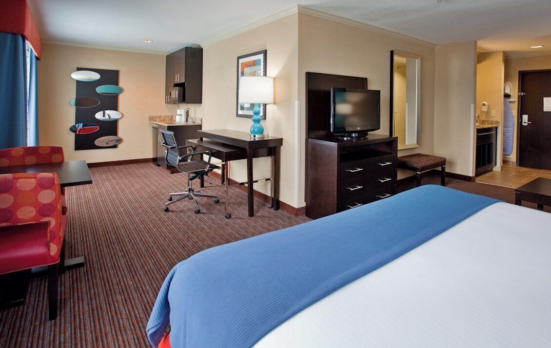 A hotel room with a bed, a desk with a chair, a television, and a seating area with a couch.