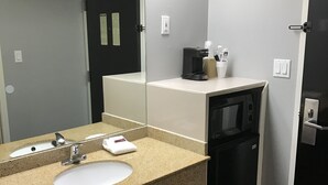 A modern bathroom with a granite countertop sink, a large mirror, and a coffee machine. - Express Inn (Weslaco)