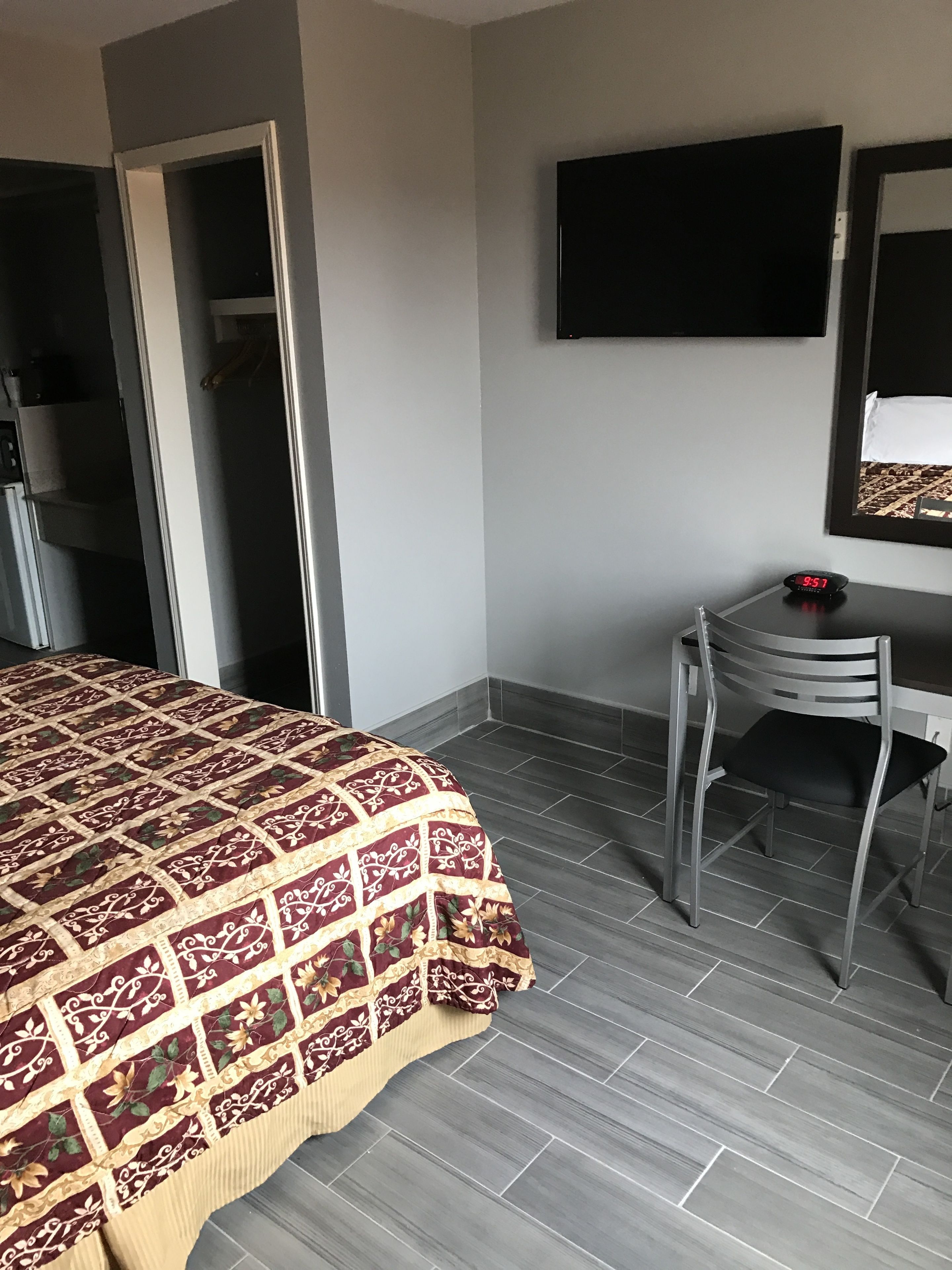 A hotel room with a bed, a desk, a chair, a TV, and a wardrobe.