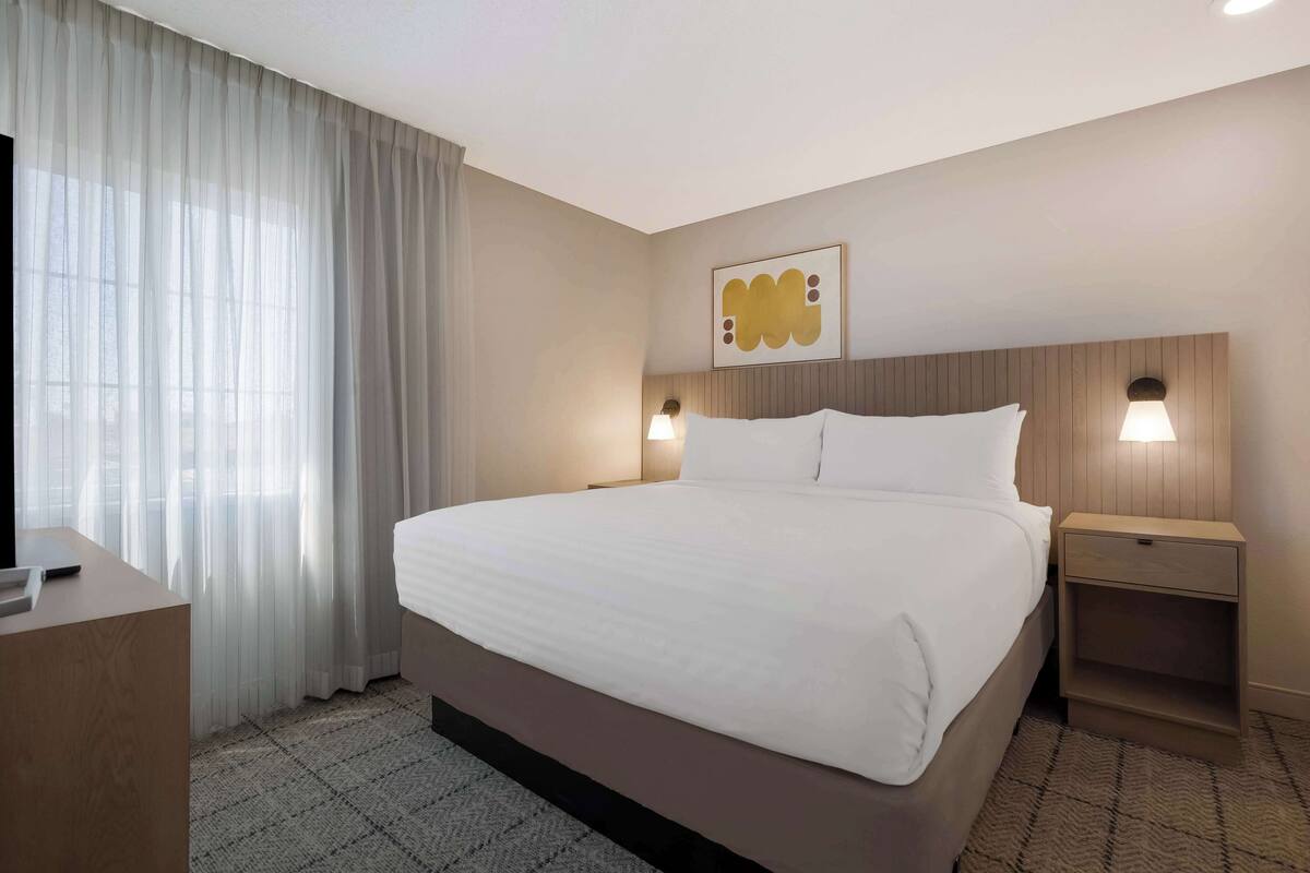Een hotelkamer met een groot bed, een bureau, een stoel, een televisie en een raam met gordijnen.