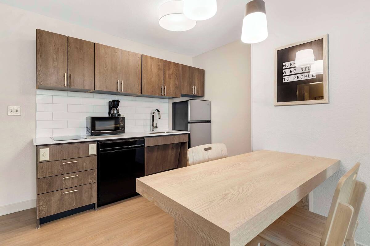 Een moderne keuken met houten kastjes, een ingebouwde magnetron, een koffiezetapparaat en een koelkast.