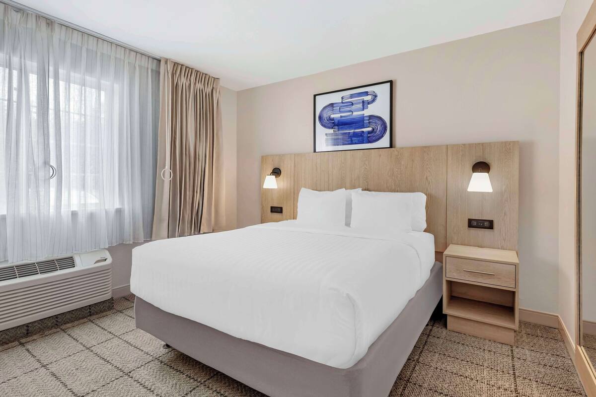 Een hotelkamer met een groot bed, een nachtkastje, een wandlamp en een raam met gordijnen.