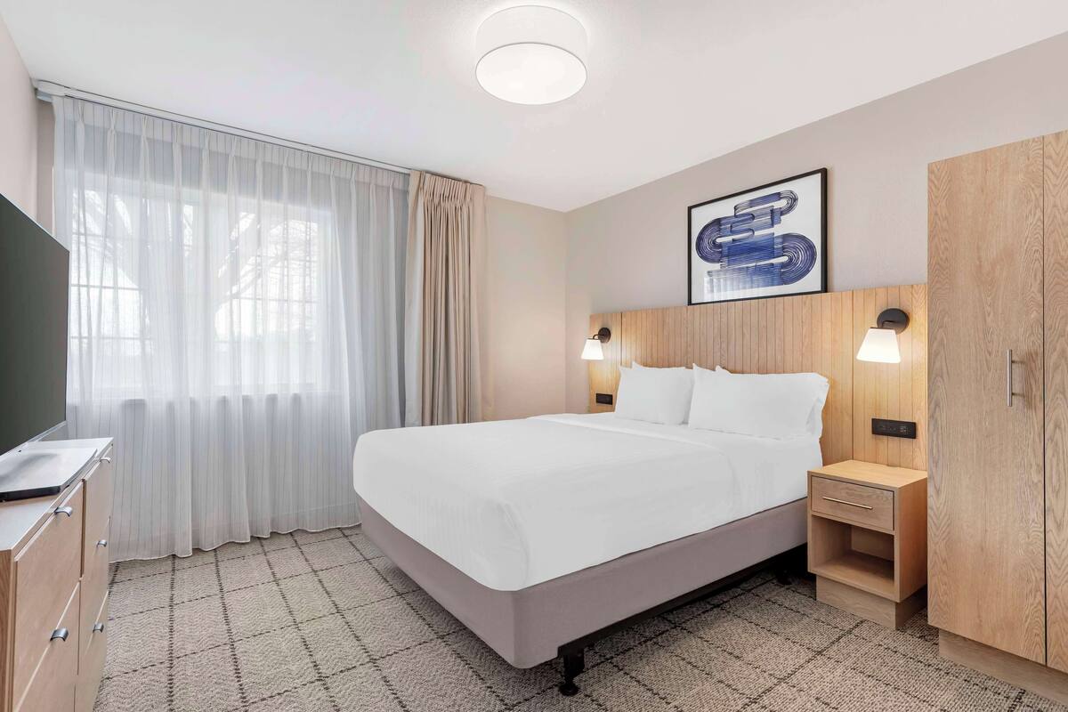 Een hotelkamer met een bed, bureau, kledingkast en een raam met gordijnen.