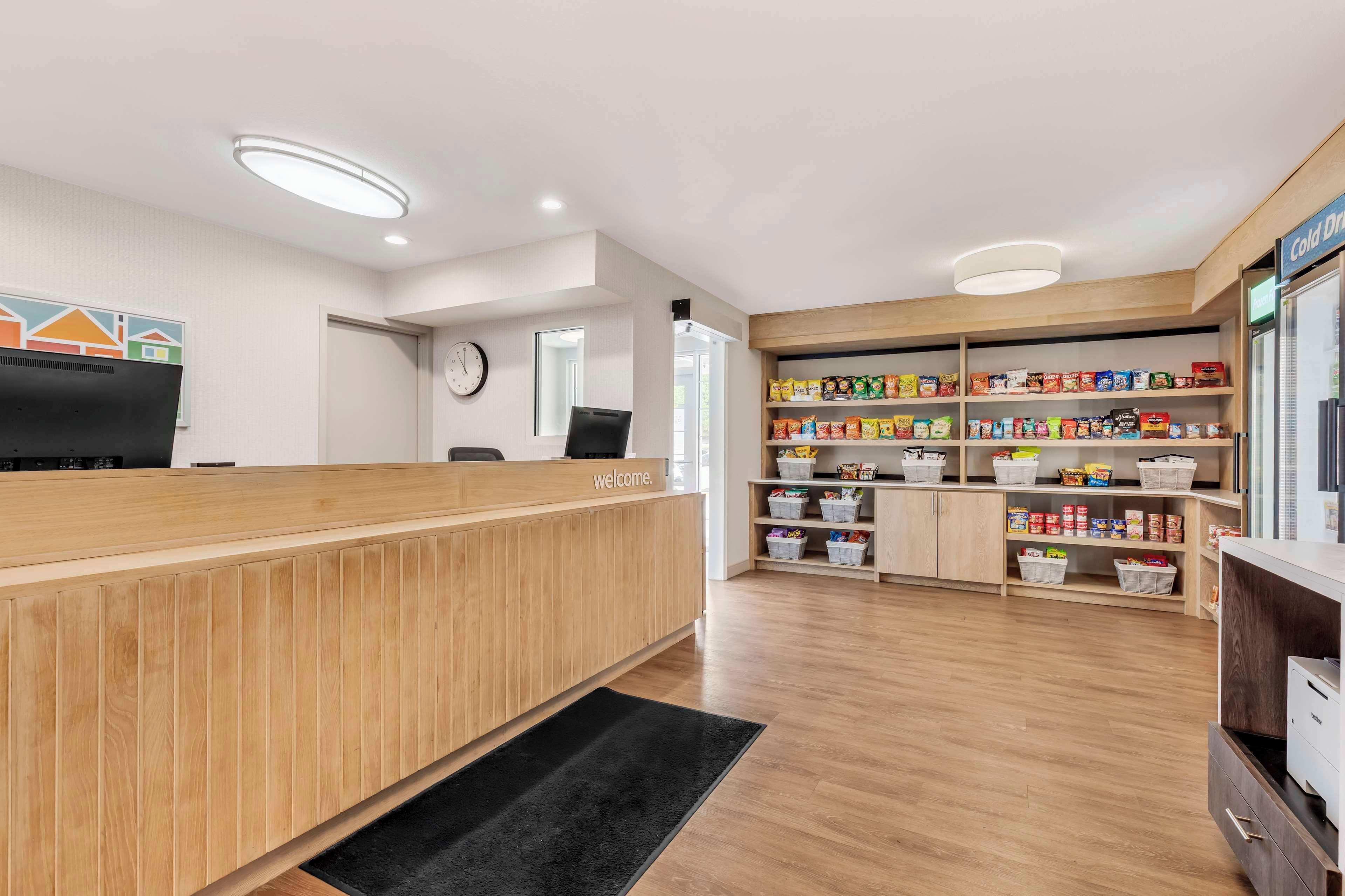 A reception area with a wooden reception desk, a clock on the wall, and shelves stocked with snacks.