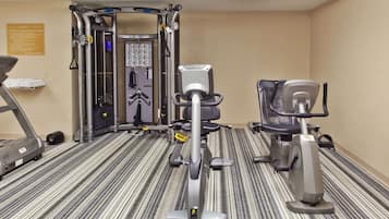 Un gimnasio con equipo de cardio, máquinas de pesas y un estante de suministros en la pared.