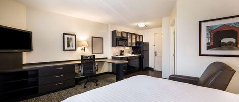 Habitación de hotel con una cama grande, un escritorio con silla, una kitchenette y un televisor.