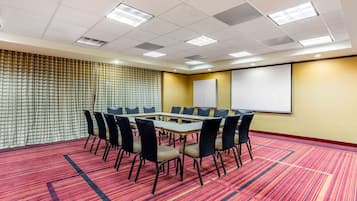 A conference room with a round table, chairs, a projector screen, and a patterned wall.