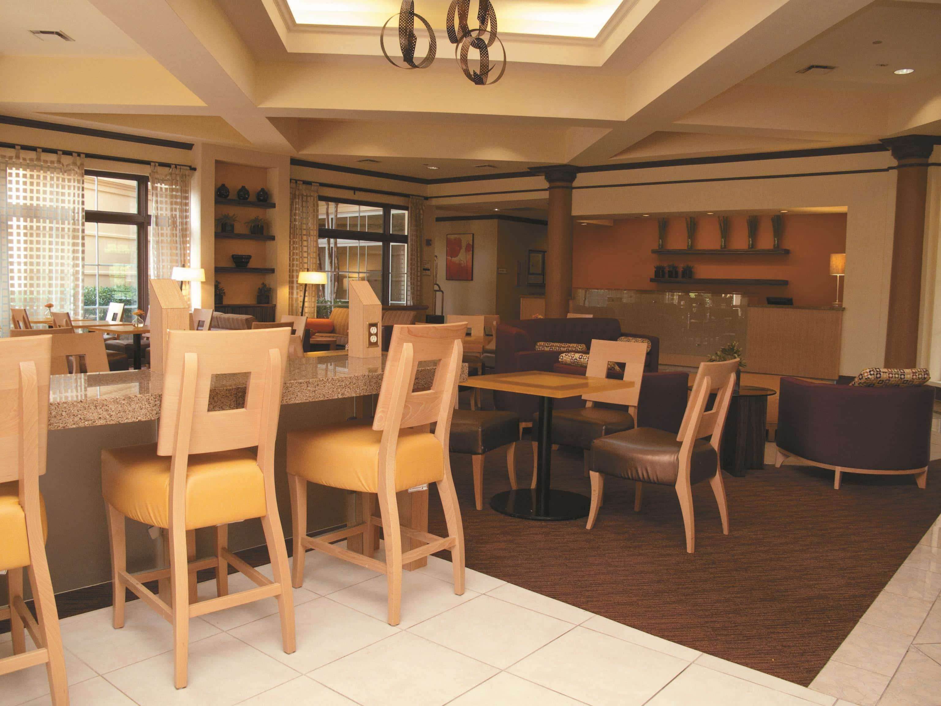 A modern hotel lobby with a dining area, seating arrangements, and a reception desk.