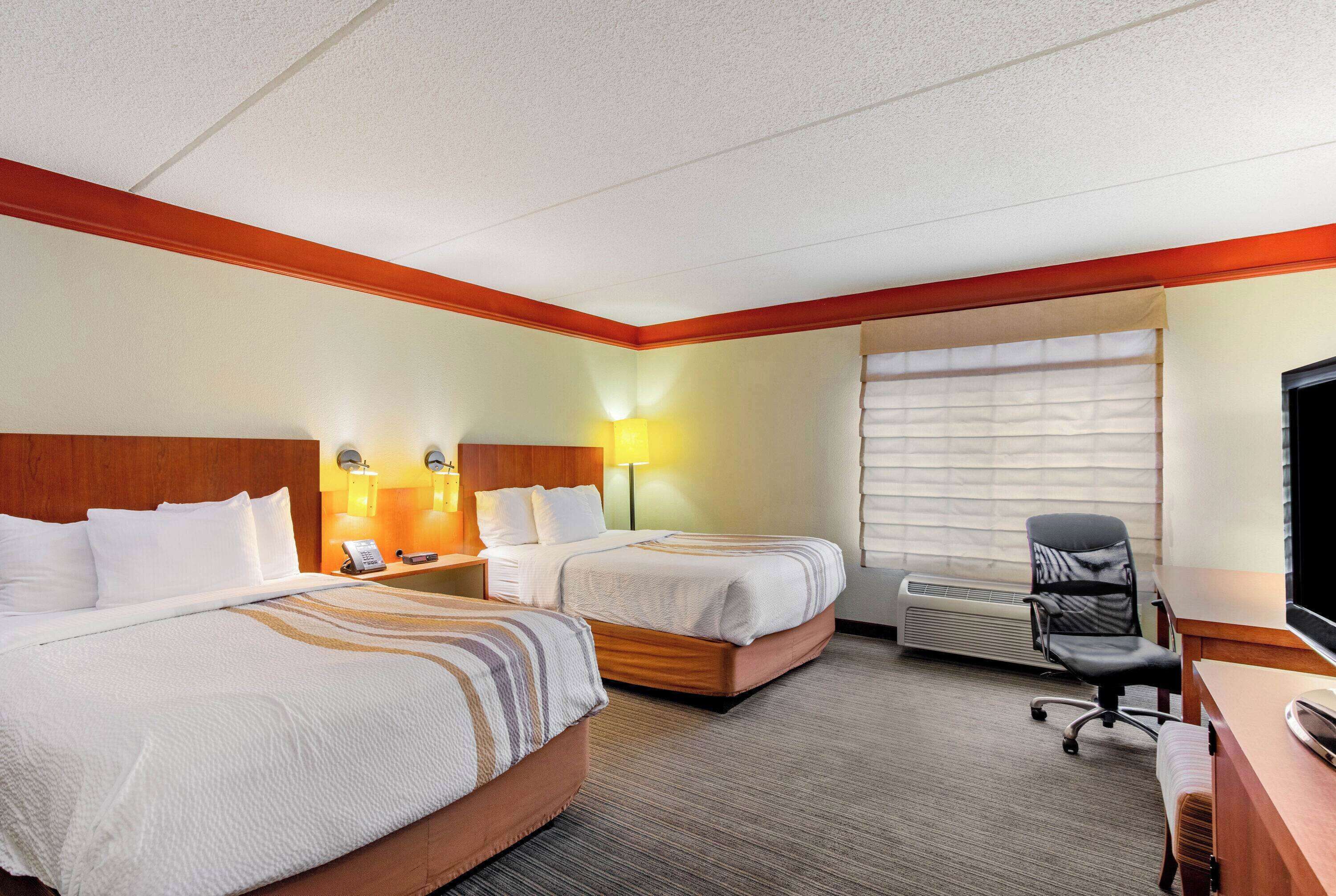 A hotel room with two beds, a desk, a chair, a TV, and a window with blinds.