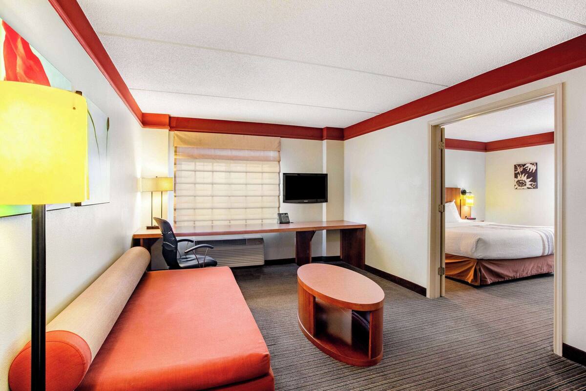 Habitación de hotel con sofá, escritorio y silla, televisión, cama y una mesita.