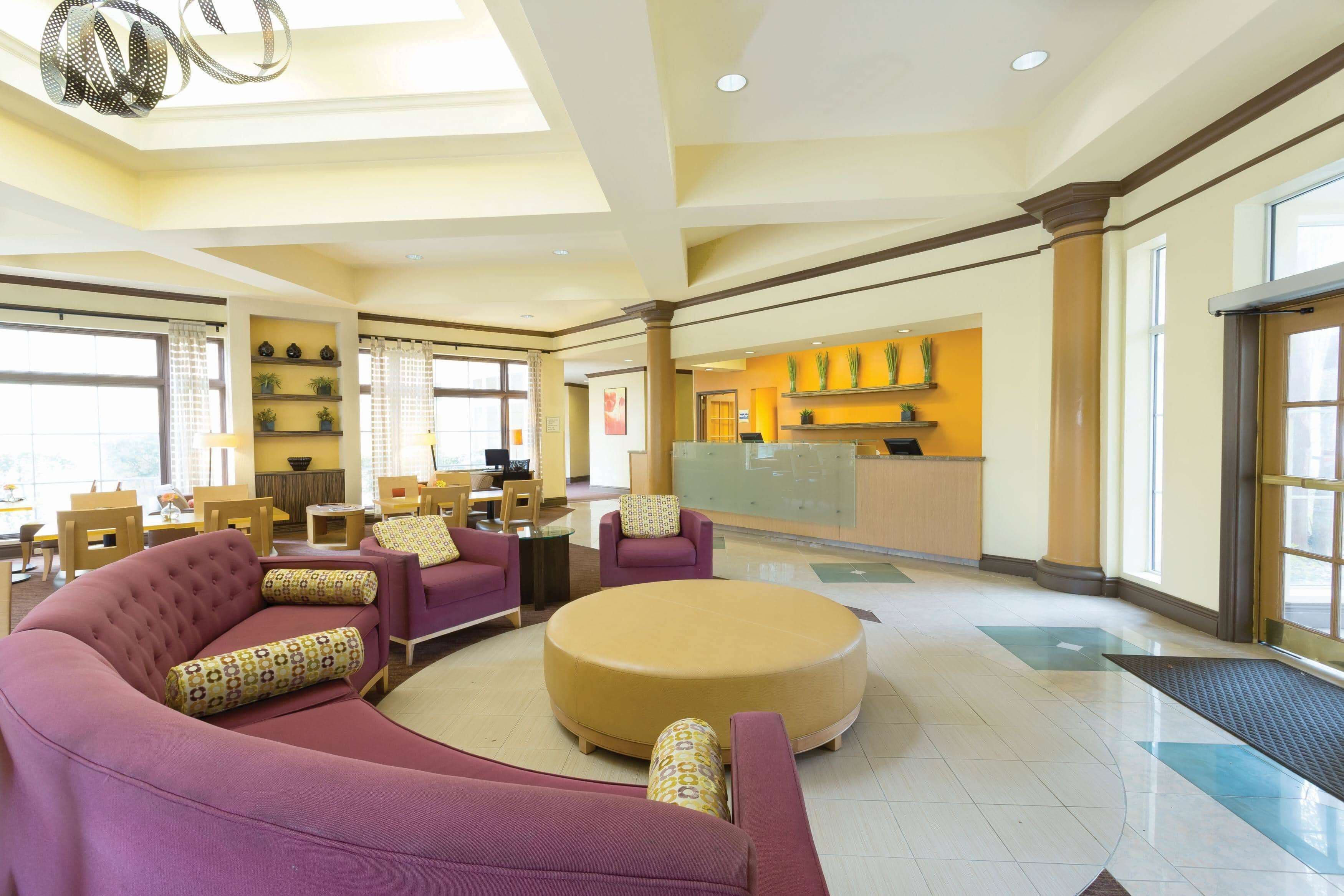 A spacious lobby with a reception desk, seating area with sofas and chairs, and a large round ottoman.
