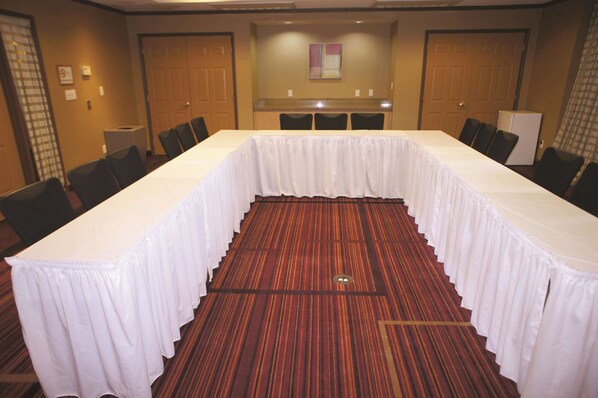 A conference room with a long table, chairs, carpeted floor, and doors. - La Quinta Inn & Suites by Wyndham Raleigh/Durham Southpoint (Durham)