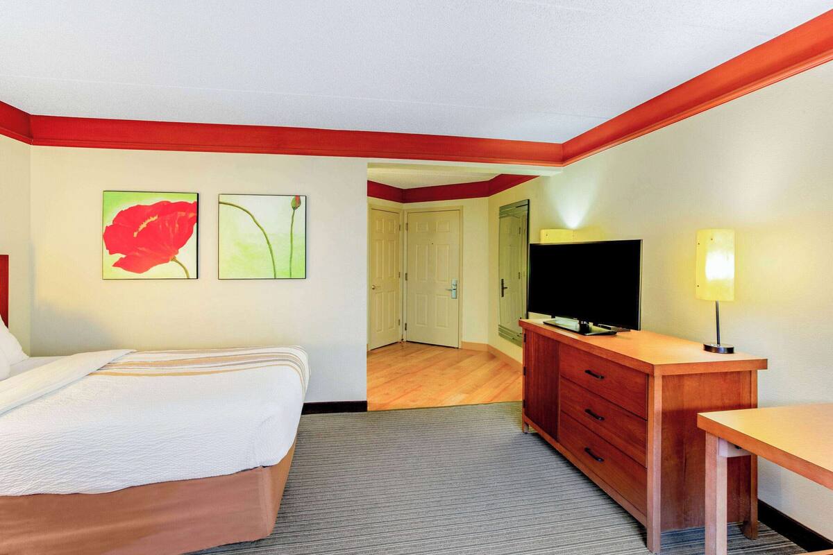 Una habitación de hotel con una cama, un aparador de madera, un televisor y obras de arte en la pared.
