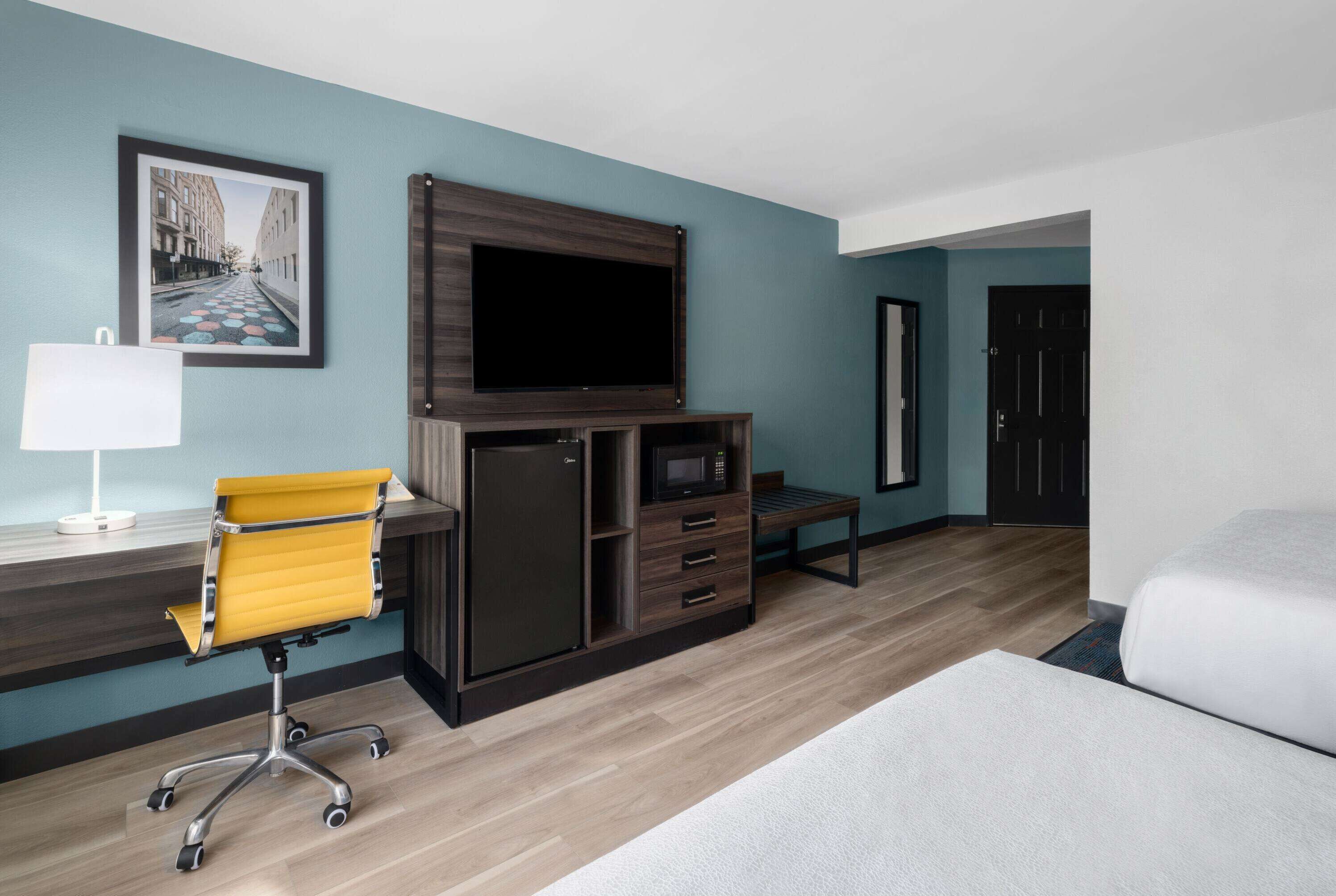A hotel room with a bed, a desk with a chair, a television, a microwave, and a refrigerator.