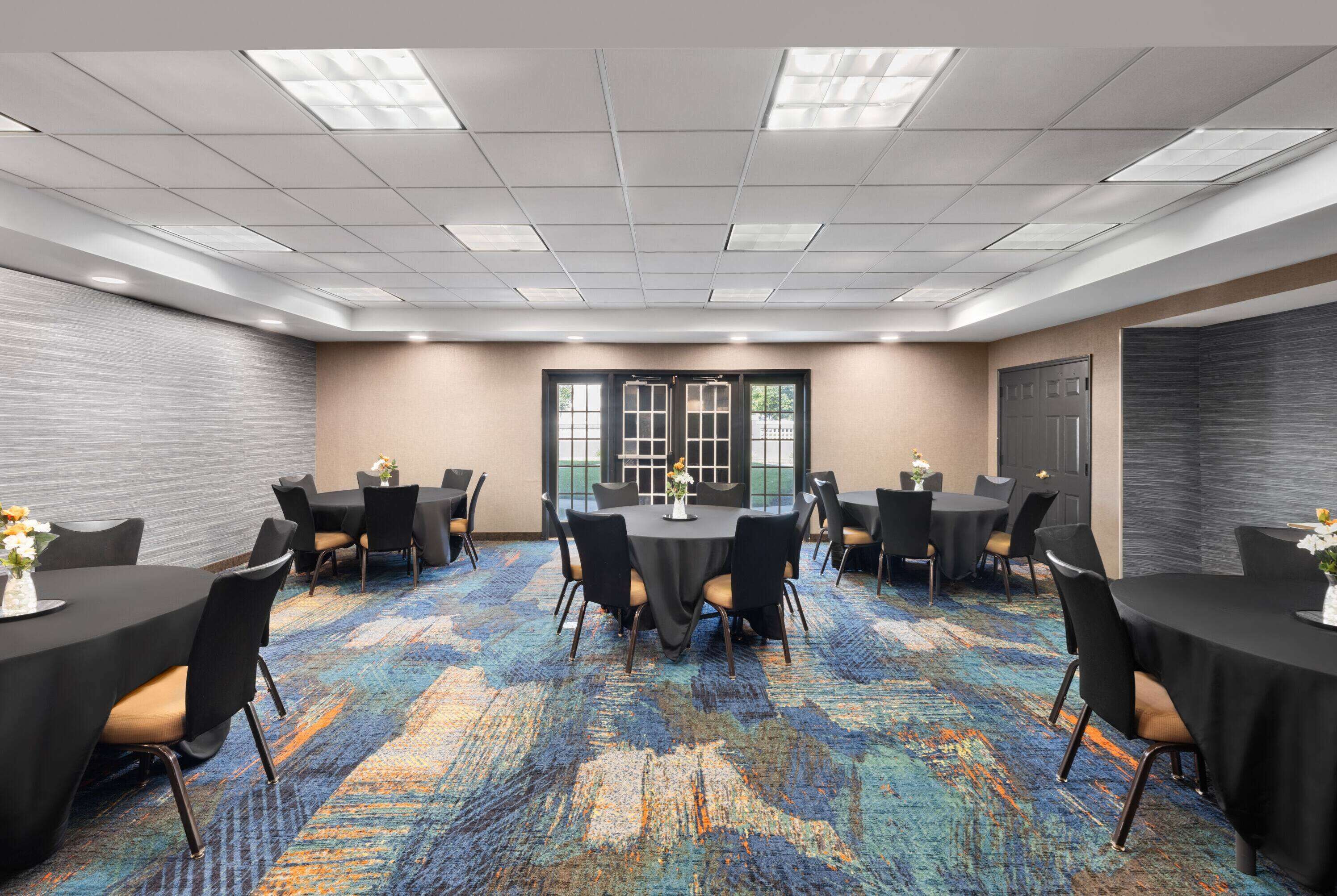 A conference room with a patterned carpet, multiple tables with chairs, and a large window with a view.