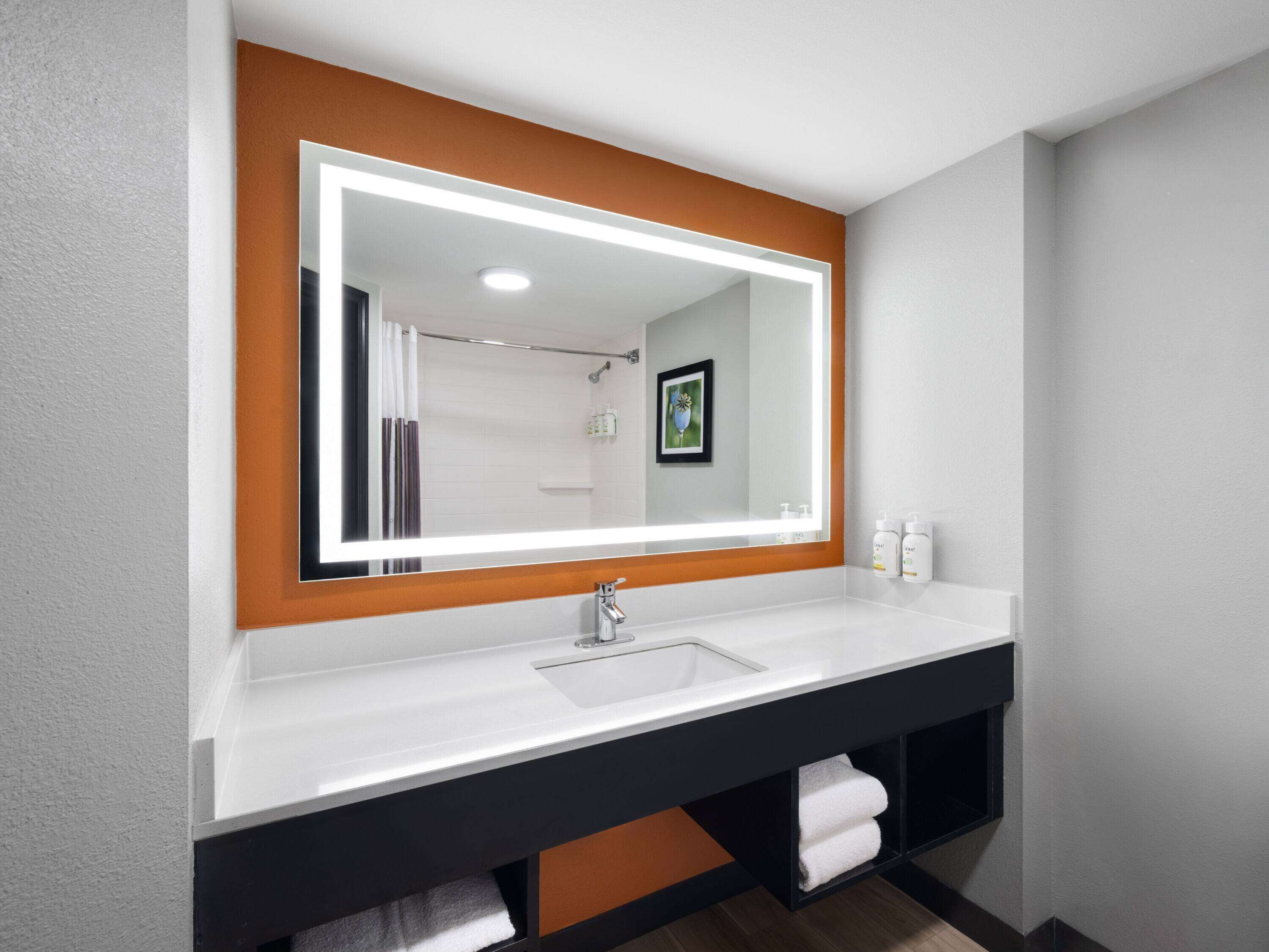 A modern bathroom with a large mirror, white sink, and black vanity.
